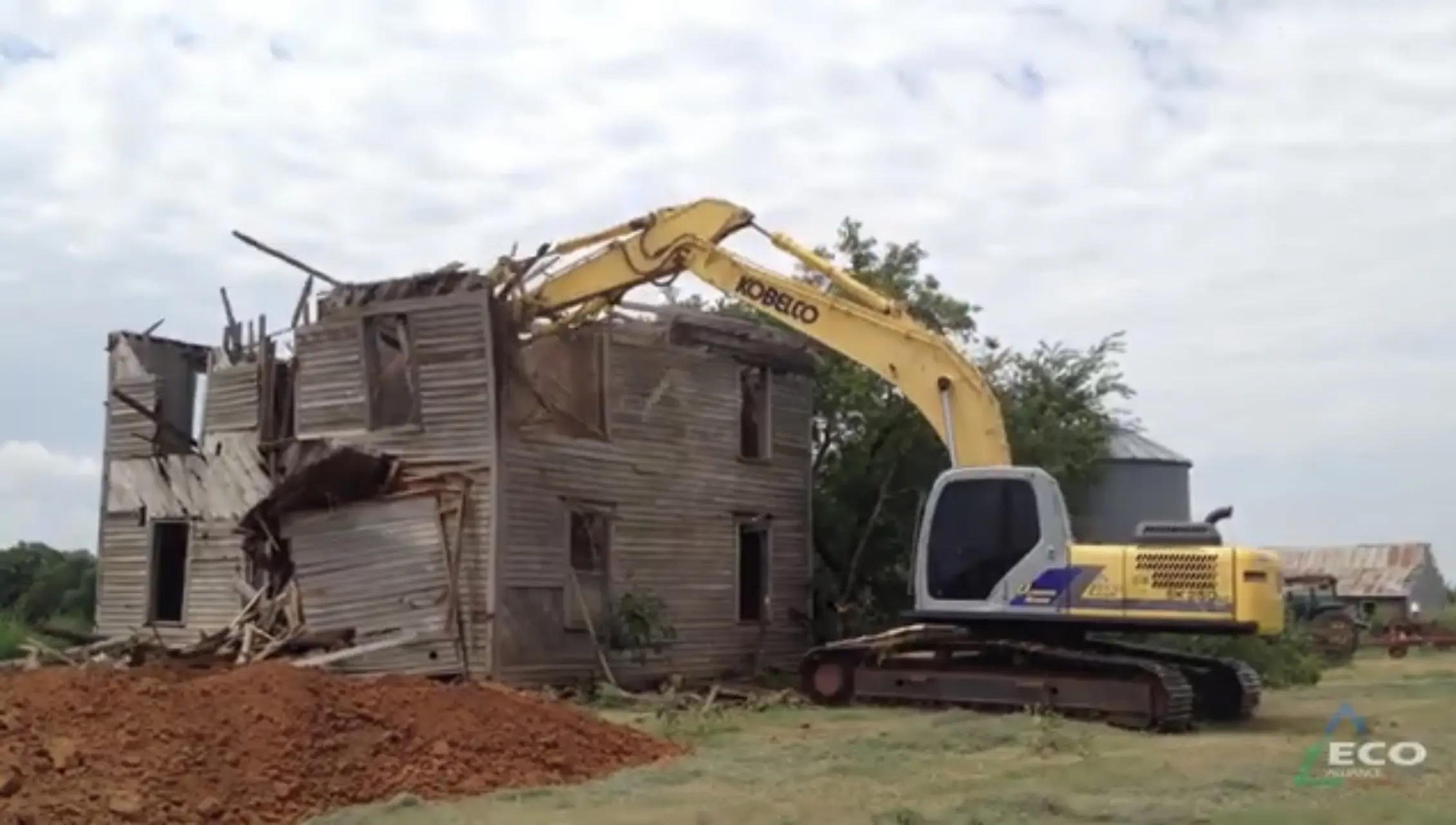 Yellow excavator demolishing dilapidated wooden house