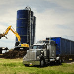 Excavator and semi-truck at farm silos