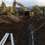 Excavator digging trench with PVC pipes