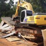 Yellow Kobelco excavator demolishing small house