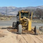 Yellow grader smoothing rural dirt road