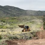 Bulldozer grading dirt road in hilly scrubland