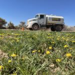 White tanker truck near field of yellow dandelions