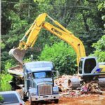 Yellow excavator loading debris into dump truck