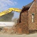 Yellow excavator demolishing brick house