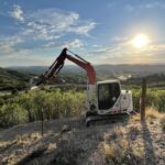 Compact excavator on hillside at sunset