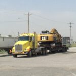 Yellow truck hauling CAT excavator on trailer