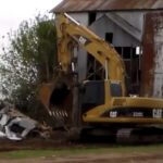 Yellow CAT excavator demolishing barn with silo