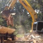 Excavator loading wood debris into truck trailer