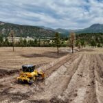 Yellow bulldozer grading field with mountain backdrop