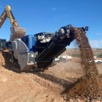 Excavator loading soil into mobile screener