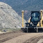 Road grader smoothing dirt road in mountains