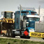Blue semi hauling bulldozer with oversize sign
