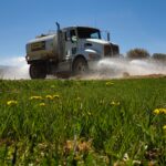 Tanker truck spraying water over grassy field