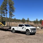 White pickup towing flatbed trailer with equipment