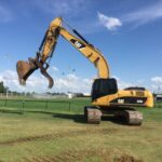Yellow CAT excavator on grassy sports field