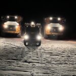 Three heavy trucks with headlights on snowy ground