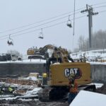 CAT excavator at snowy construction site, ski-lifts
