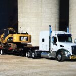 White semi hauling CAT excavator on lowboy trailer