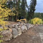 Yellow compact track loader on rock retaining wall